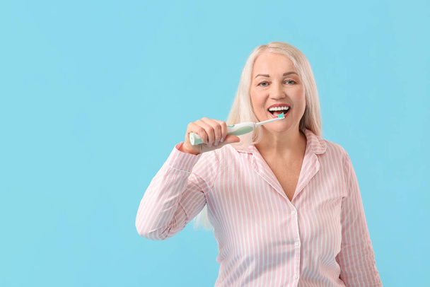 Reife Frau beim Zähneputzen auf farbigem Hintergrund - Foto, Bild