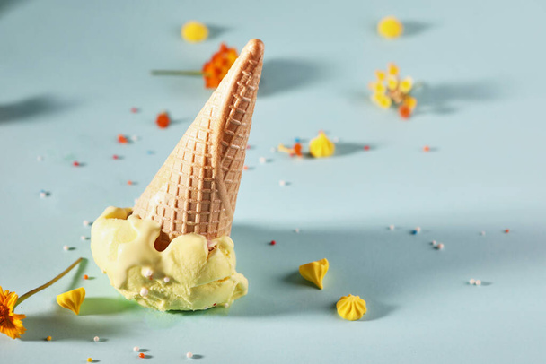 Orange ice cream with waffle cone on blue background with yellow flowers. - Foto, Imagen