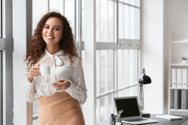 Beautiful young woman drinking coffee in office - Zdjęcie, obraz