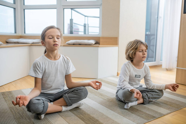 Kids doing yoga together at home and sitting in meditation - Fotoğraf, Görsel