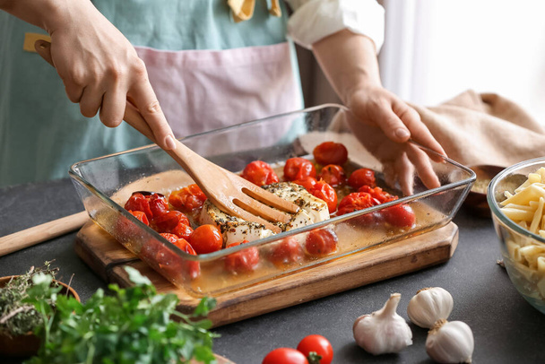 Woman preparing tomatoes and feta cheese in kitchen - Φωτογραφία, εικόνα