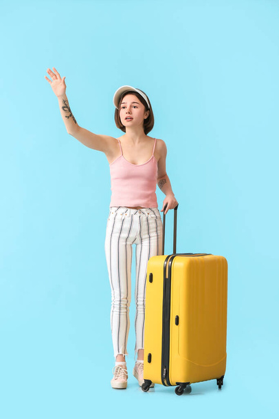 Young woman with suitcase hitchhiking on color background - Foto, Imagen