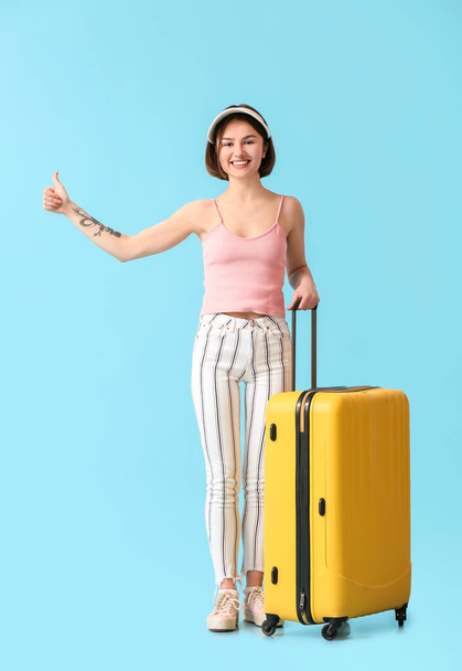 Young woman with suitcase hitchhiking on color background - Foto, imagen