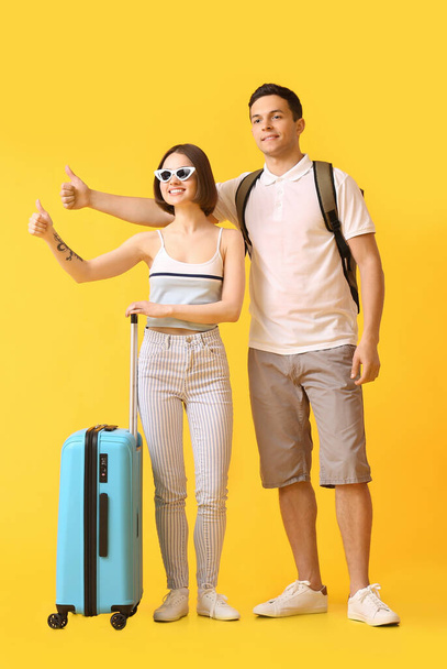 Young couple with suitcase hitchhiking on color background - Foto, Imagem