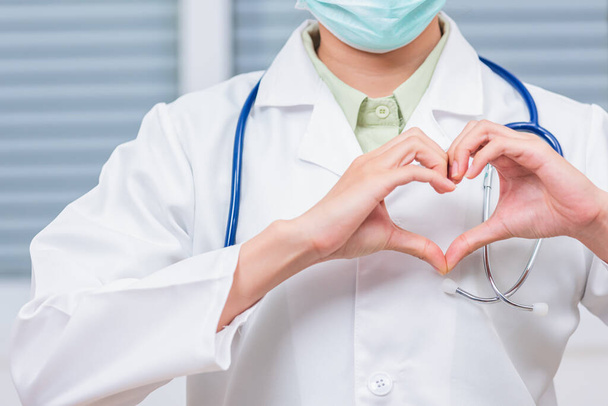Closeup of doctor woman wearing white coat standing making heart finger shape, Doctor's hand sign, Healthy medical heart coronavirus concept - Foto, Bild