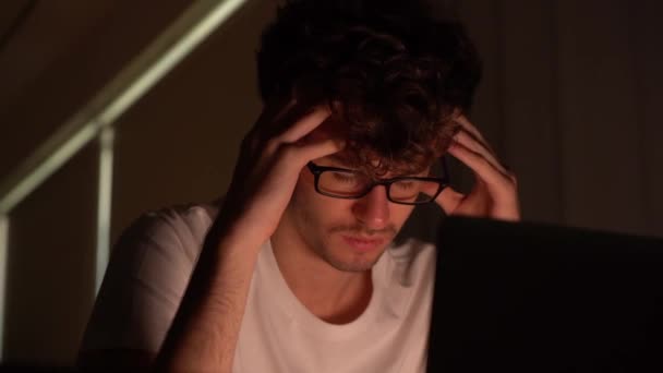 κουρασμένος άνθρωπος κάθεται με τα χέρια στο κεφάλι του μπροστά από έναν φορητό υπολογιστή με άγχος και εξαντληθεί πάνω από εργάστηκε αργά το βράδυ. - Πλάνα, βίντεο