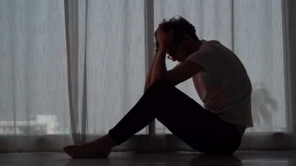 Verzweifelter Mann sitzt wegen Stress und Depressionen mit den Händen auf dem Boden neben Fenstern. - Filmmaterial, Video