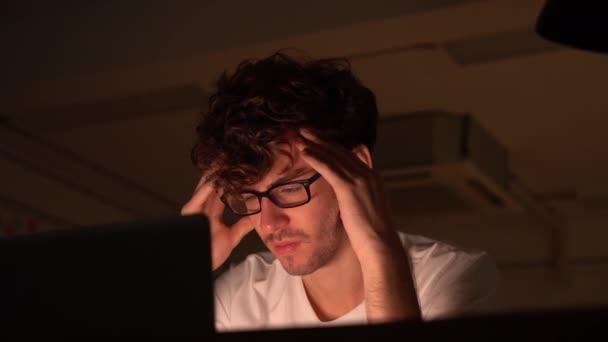 tired man sitting with hands on his head in front of a laptop computer with stress and exhausted over worked late at night. - Footage, Video