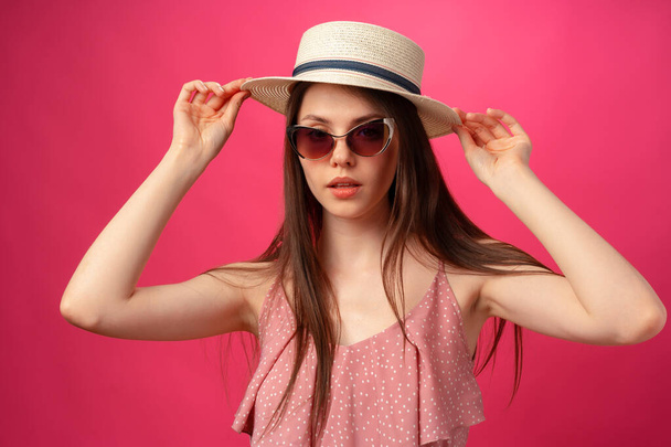 Studio fashion portrait of a young attractive woman in hat and glasses against pink backgorund - Foto, immagini