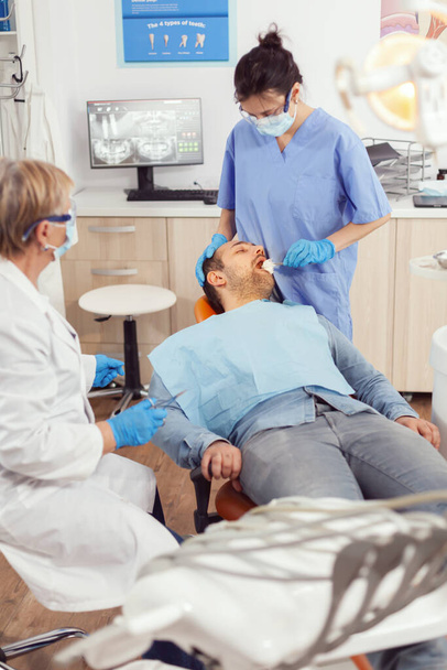 Медсестра-стоматолог ищет во рту пациента, готовясь к стоматологической операции - Фото, изображение