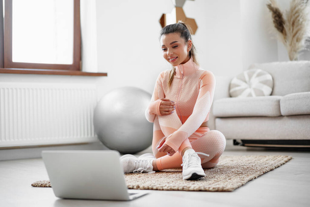 Giovane donna in abbigliamento sportivo utilizzando il computer portatile per guardare video tutorial di allenamento a casa - Foto, immagini