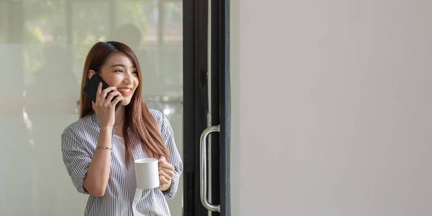 Sonriendo mujer asiática hablando por teléfono en casa, la joven feliz sostiene el teléfono celular haciendo llamada de contestación, adolescente atractivo teniendo una conversación agradable charlando por móvil con un amigo. - Foto, imagen