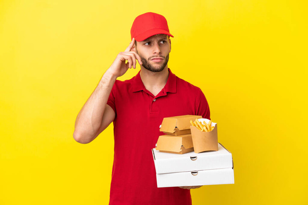 repartidor de pizza recogiendo cajas de pizza y hamburguesas sobre un fondo aislado teniendo dudas y pensando - Foto, Imagen