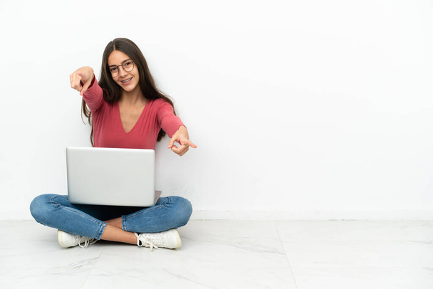 Giovane ragazza francese seduta sul pavimento con il suo computer portatile punti dito a voi sorridendo - Foto, immagini