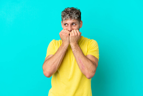 Young handsome caucasian man isolated on blue background nervous and scared putting hands to mouth - Fotoğraf, Görsel
