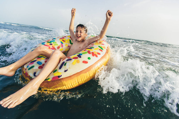 Fröhliches Kind auf aufblasbarem Ring auf brechender Welle. Lebensstil, Schwimmen. Selektiver Fokus - Foto, Bild