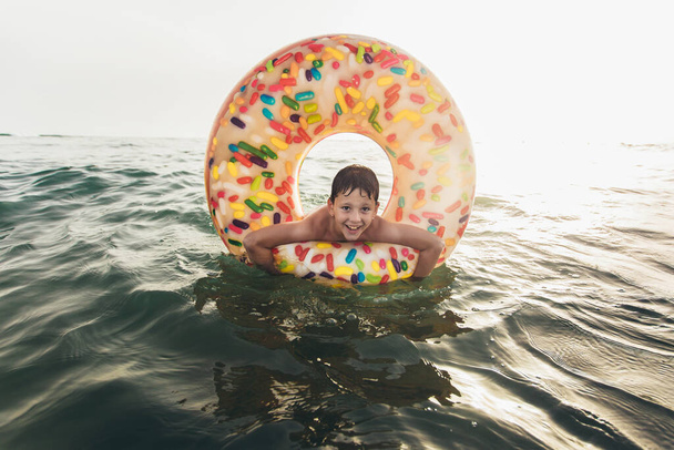 Fröhliches Kind auf aufblasbarem Ring auf brechender Welle. Lebensstil, Schwimmen. Selektiver Fokus - Foto, Bild