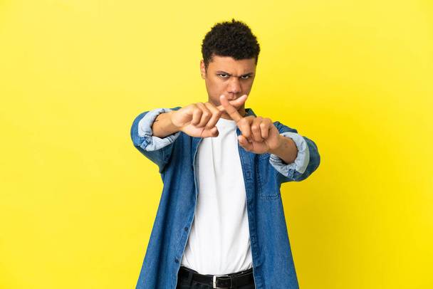 Joven hombre afroamericano aislado sobre fondo amarillo haciendo gesto de stop con su mano para detener un acto - Foto, Imagen