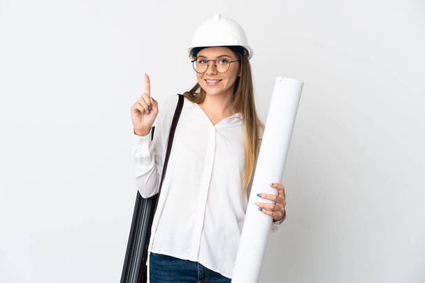 Młoda litewska architekt kobieta w kasku i trzymając odizolowane na białym tle plany pokazujące i podnoszące palec w znak najlepszych - Zdjęcie, obraz