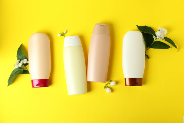 Blanco flessen shampoo en bloemen op gele achtergrond - Foto, afbeelding