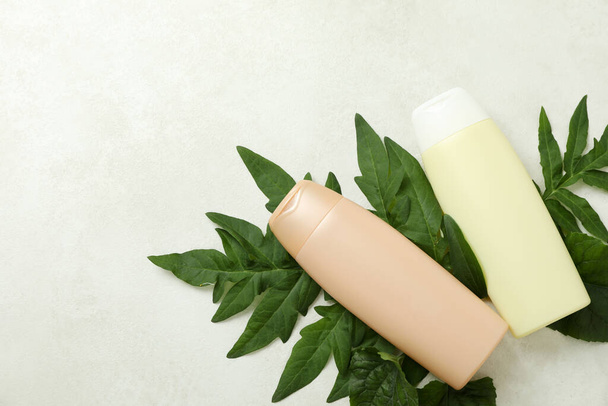 Пустые бутылки шампуня и листья на белом текстурированном фоне - Фото, изображение