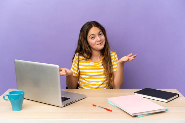 Menina estudante em um local de trabalho com um laptop isolado no fundo roxo feliz e sorridente - Foto, Imagem