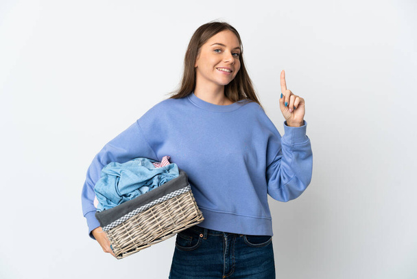 Young Lithuanian woman holding a clothes basket isolated on white background showing and lifting a finger in sign of the best - Fotó, kép