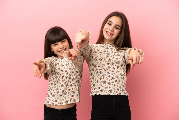 Οι μικρές αδερφές που είναι απομονωμένες σε ροζ φόντο σε δείχνουν χαμογελώντας. - Φωτογραφία, εικόνα
