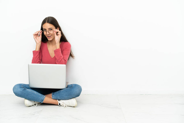 Jovem francesa sentada no chão com seu laptop com óculos e surpreso - Foto, Imagem
