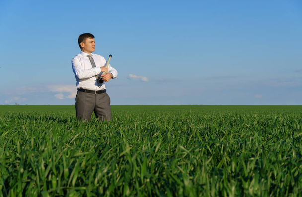 бізнесмен позує зі склом, він дивиться на відстань і шукає щось, зелену траву і блакитне небо як фон
 - Фото, зображення