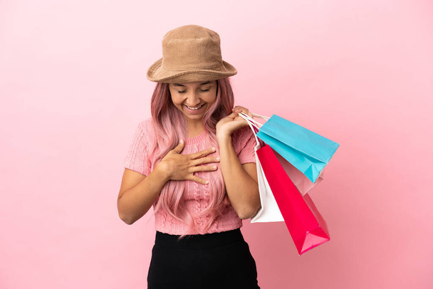 jong gemengd ras vrouw met boodschappentas geïsoleerd op roze achtergrond glimlachen veel - Foto, afbeelding