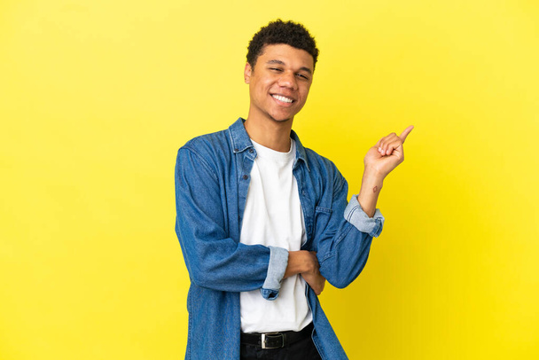 Junger afroamerikanischer Mann isoliert auf gelbem Hintergrund glücklich und zeigt nach oben - Foto, Bild