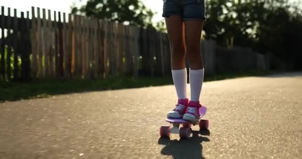 Mała dziewczynka uczy się jeździć na deskorolce, anonimowe dziecko w białych skarpetkach i różowych butach jeżdżące na deskorolce na wiejskiej ulicy letniego miasta. - Materiał filmowy, wideo