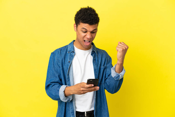 Young African American man isolated on yellow background surprised and sending a message - Zdjęcie, obraz