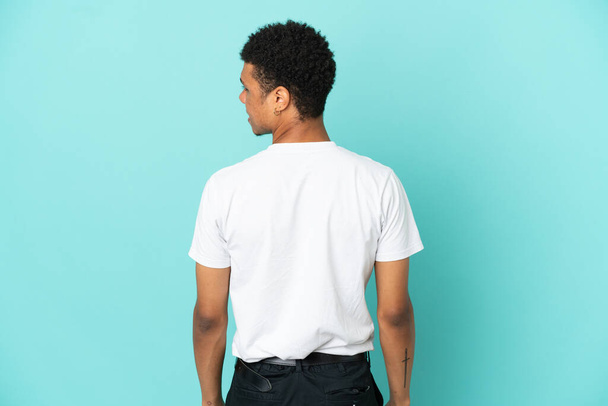 Junger afroamerikanischer Mann isoliert auf blauem Hintergrund in Rückenlage und seitlich schauend - Foto, Bild