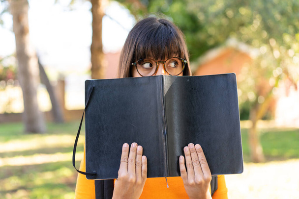 Joven estudiante en un parque sosteniendo un cuaderno - Foto, imagen