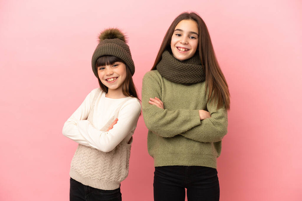 Kleine Schwestern tragen Winterkleidung isoliert auf rosa Hintergrund und halten die Arme in Frontalposition gekreuzt - Foto, Bild