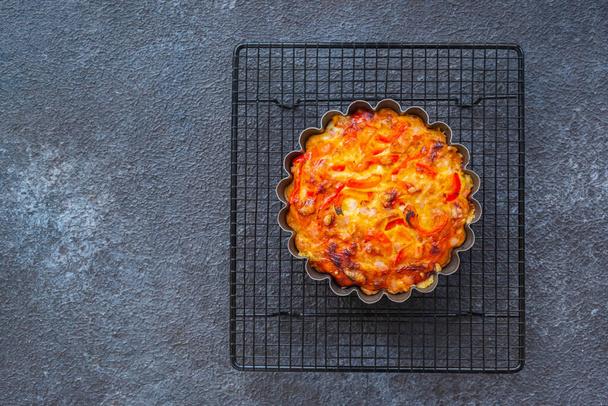 Unsweetened pie or mini tart with egg, chicken, bell pepper and cheese on a black wire rack on a black concrete background. Savory pastries - Foto, imagen