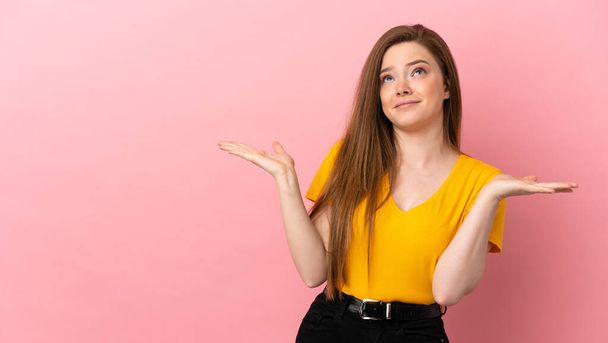 tiener meisje over geïsoleerde roze achtergrond maken twijfels gebaar - Foto, afbeelding