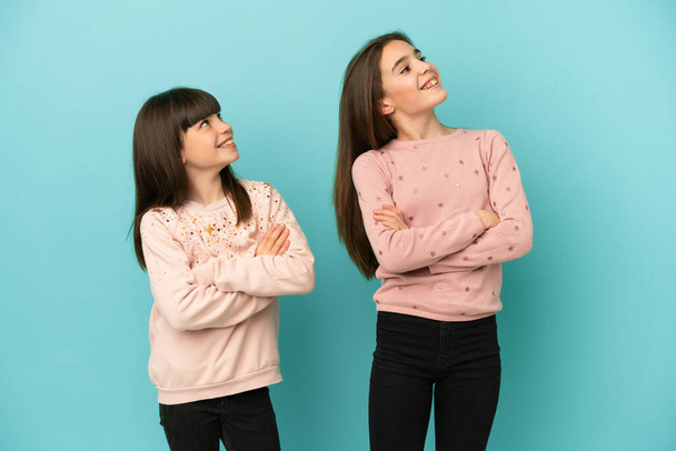 Kleine Schwestern Mädchen isoliert auf blauem Hintergrund schauen auf, während sie lächeln - Foto, Bild