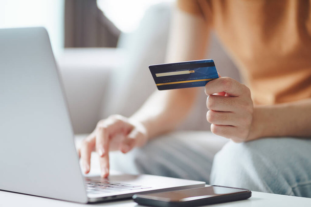 Een jonge vrouw met een creditcard en een laptop. Online winkelen, internetbankieren, e-commerce, geld uitgeven, thuiswerken - Foto, afbeelding