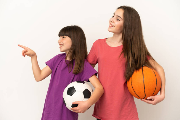 Little sisters playing football and basketball isolated on white background presenting an idea while looking smiling towards - Photo, Image