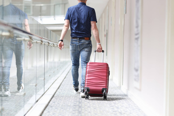 Πίσω όψη του άνδρα τραβώντας βαλίτσα κάτω από το διάδρομο του ξενοδοχείου - Φωτογραφία, εικόνα