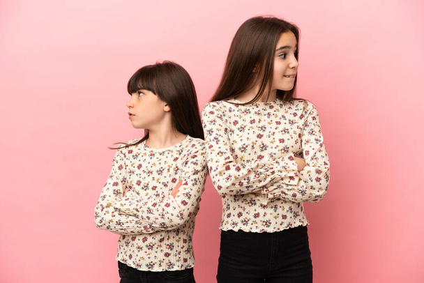 Kleine zusjes meisjes geïsoleerd op roze achtergrond met verwarde gezicht uitdrukking terwijl beten lip - Foto, afbeelding