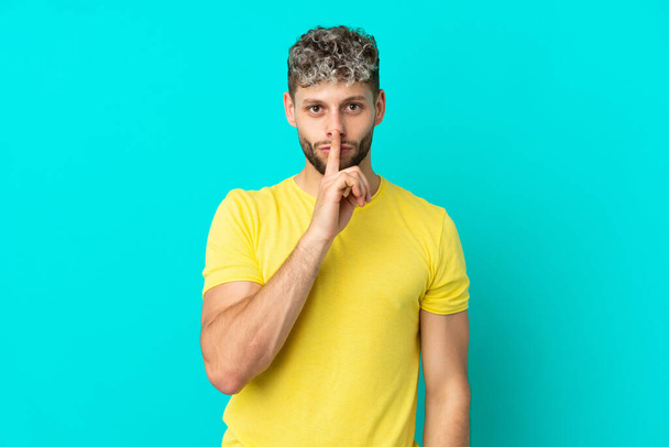 Young handsome caucasian man isolated on blue background showing a sign of silence gesture putting finger in mouth - Foto, Imagen