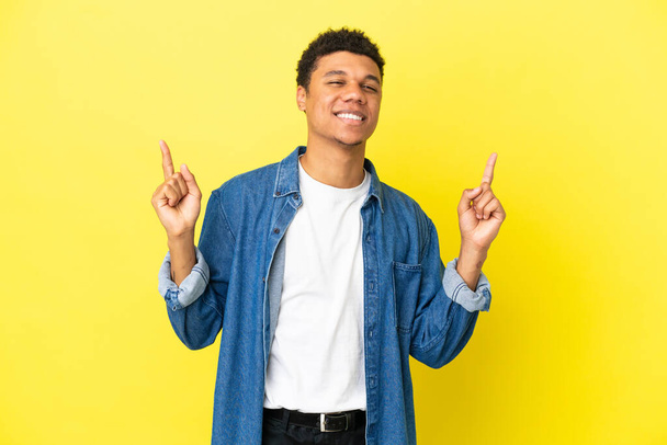 Jonge Afro-Amerikaanse man geïsoleerd op gele achtergrond wijzend op een geweldig idee - Foto, afbeelding