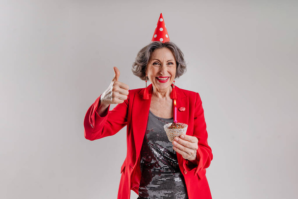 Idősebb nő kezében születésnapi torta gyertyával visel party kalap - Fotó, kép