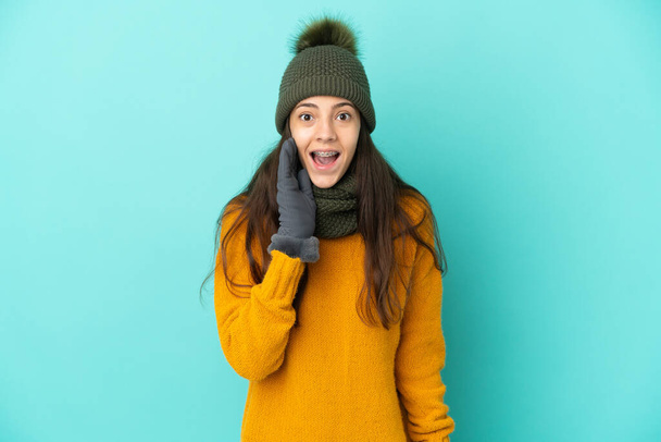 Jeune fille française isolée sur fond bleu avec chapeau d'hiver avec surprise et expression faciale choquée - Photo, image