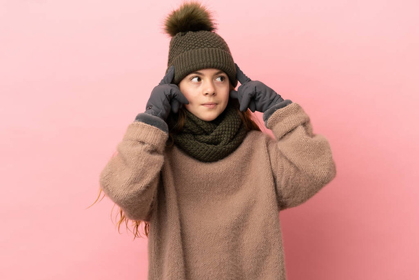 Kış şapkalı küçük kız pembe arka planda izole edilmiş kuşkuları ve düşünceleri var. - Fotoğraf, Görsel