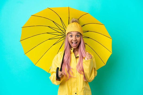 Молодая женщина смешанной расы в непромокаемом плаще и зонтике празднует победу на позиции победителя - Фото, изображение